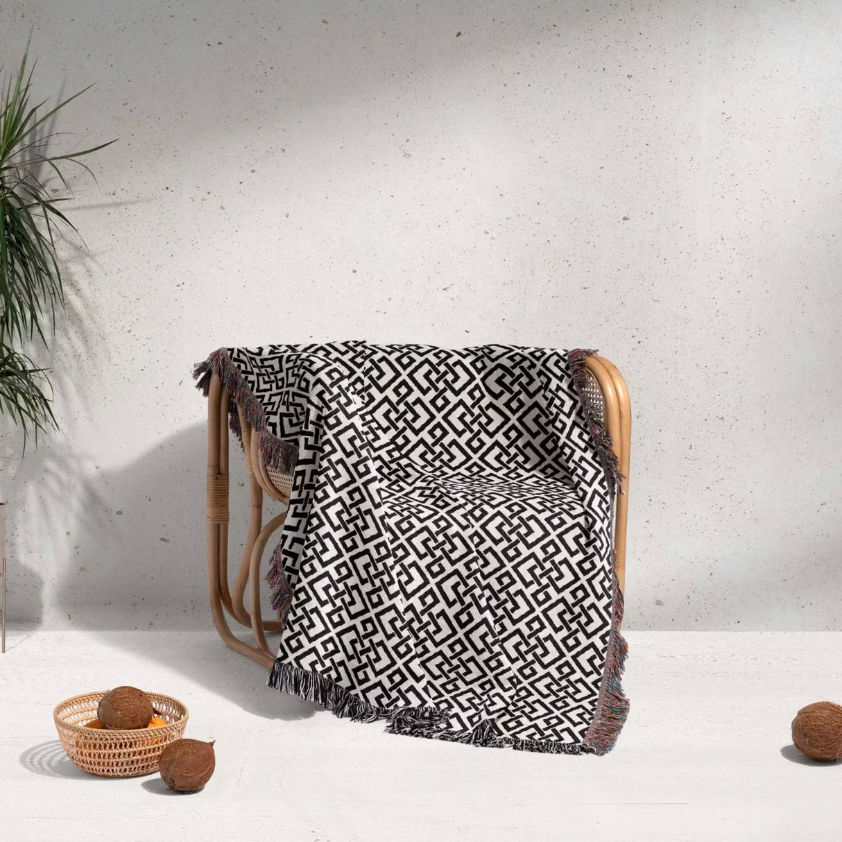 Black and white luxury geometric patterned woven blanket throw tapestry over a chair against a light gray wall.