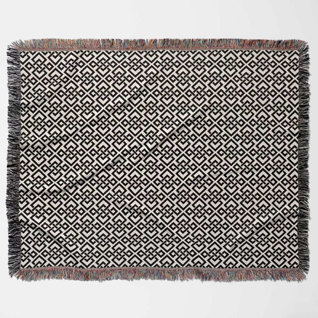 Black and white luxury geometric patterned woven blanket throw tapestry with fringed edges flat lay on a light gray background