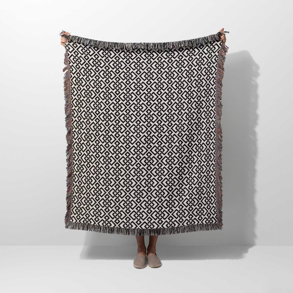 Black and white luxury geometric patterned woven blanket throw tapestry with fringes held by a person on a white background