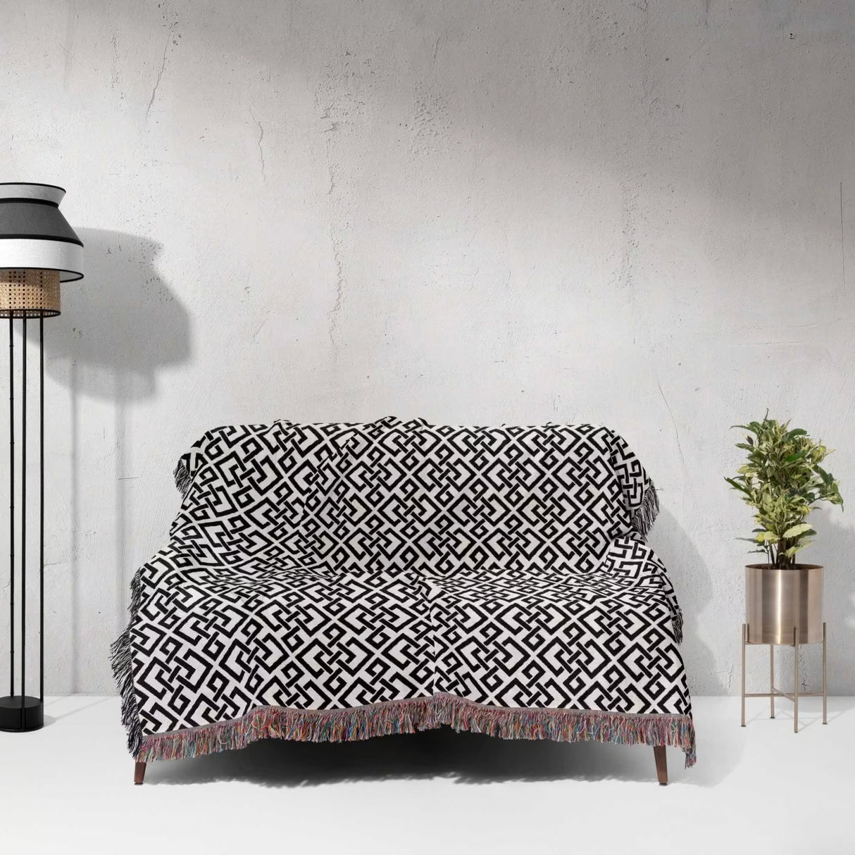 Black and white luxury geometric patterned woven blanket throw tapestry on a couch against a white wall with a lamp and plant in the background.