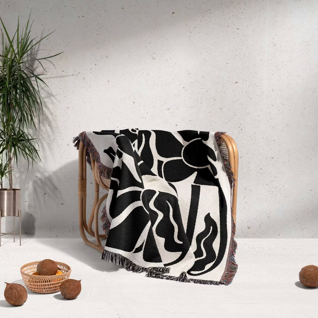 Matisse style black and white botanical cotton woven throw blanket draped over a chair against a light gray wall.