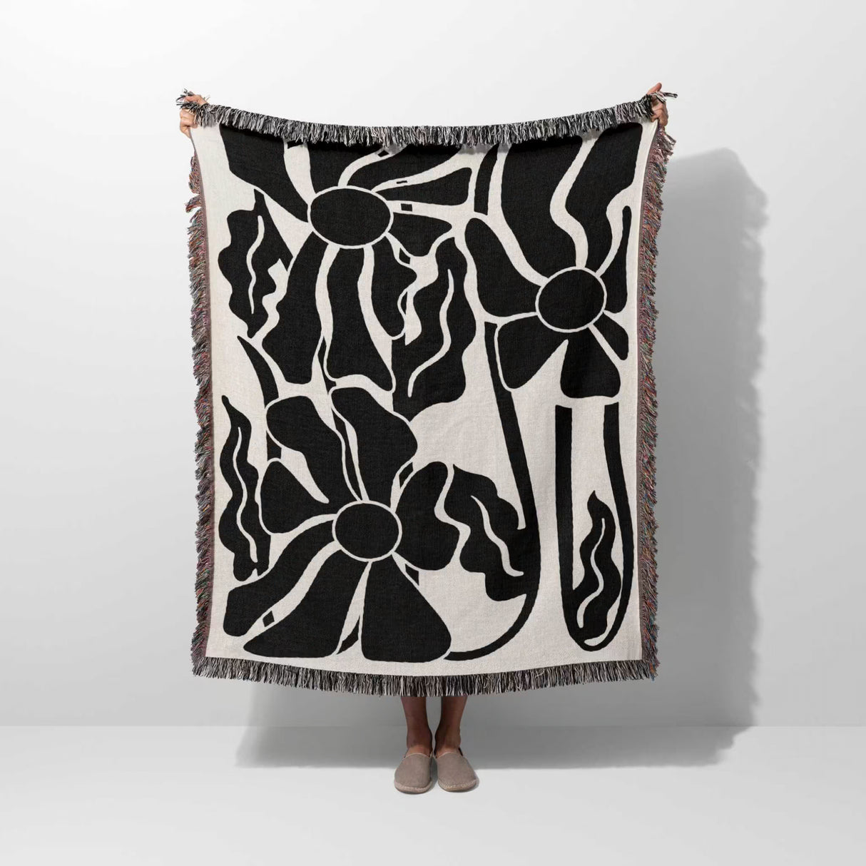Matisse style black and white botanical cotton woven throw blanket draped over a person on a white background