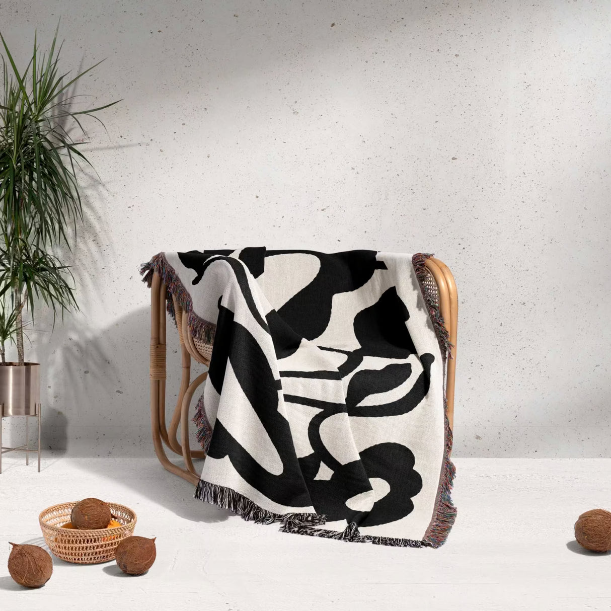 Matisse style black and white cotton woven throw blanket draped over a wooden chair against a light gray wall.