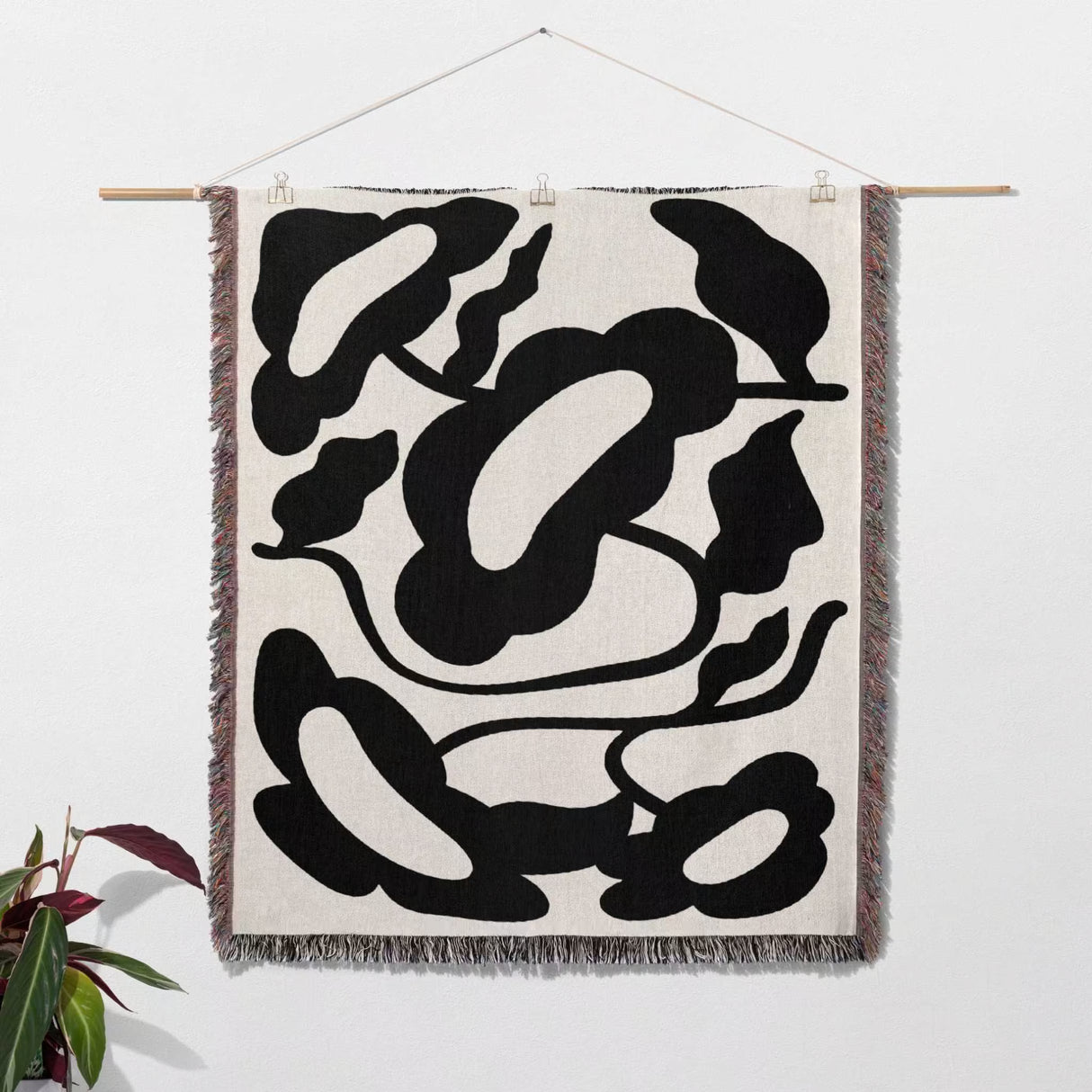 Matisse style black and white cotton woven throw blanket tapestry hanging on a white wall with a plant in the corner.