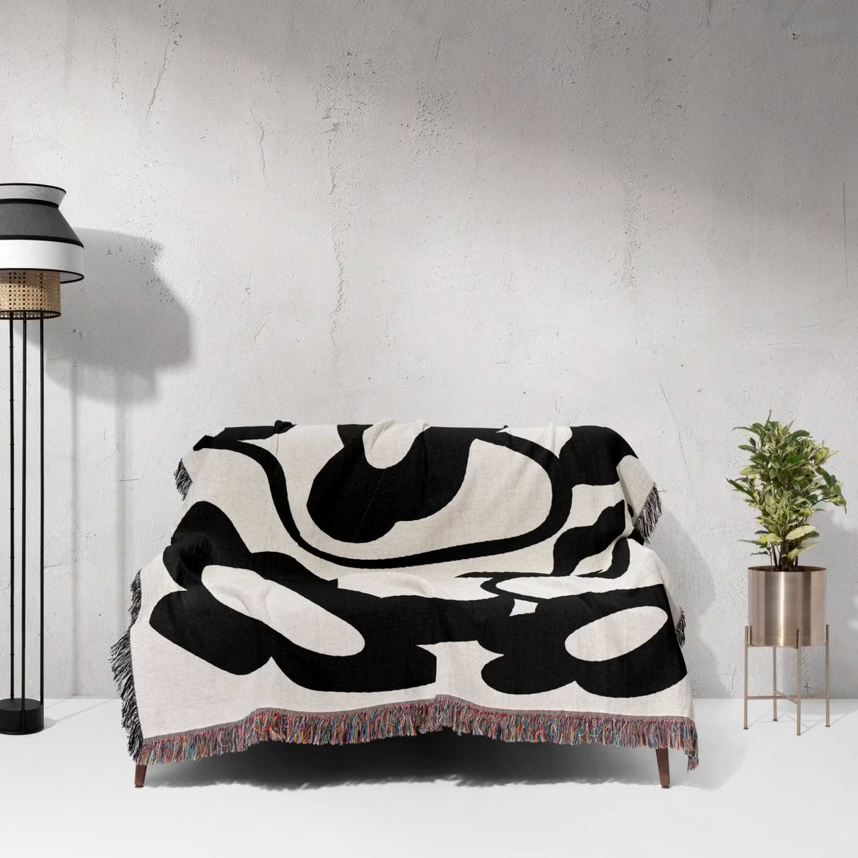 Matisse style black and white cotton woven throw blanket draped over a couch against a white wall.