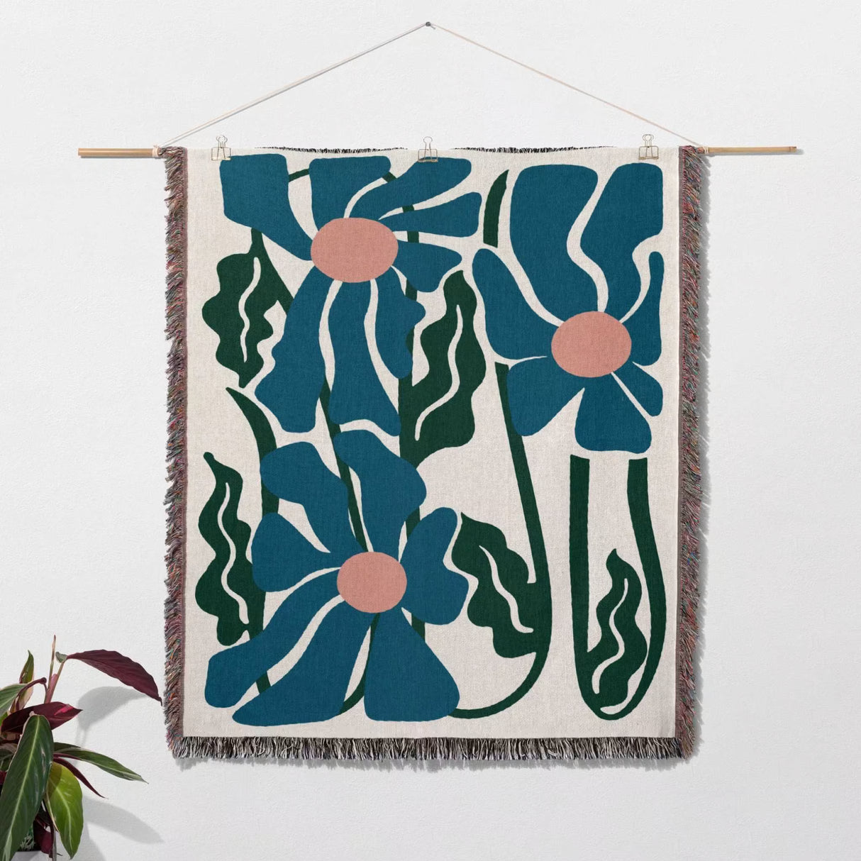 Floral patterned Matisse style blue flowers cotton woven throw blanket with blue flowers and green leaves on a white wall.