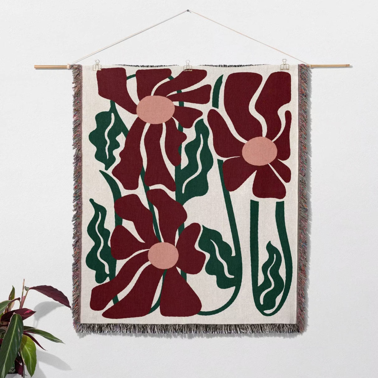 Floral patterned Matisse style blue pure cotton woven throw blanket tapestry hanging on a white wall with a plant on the side.