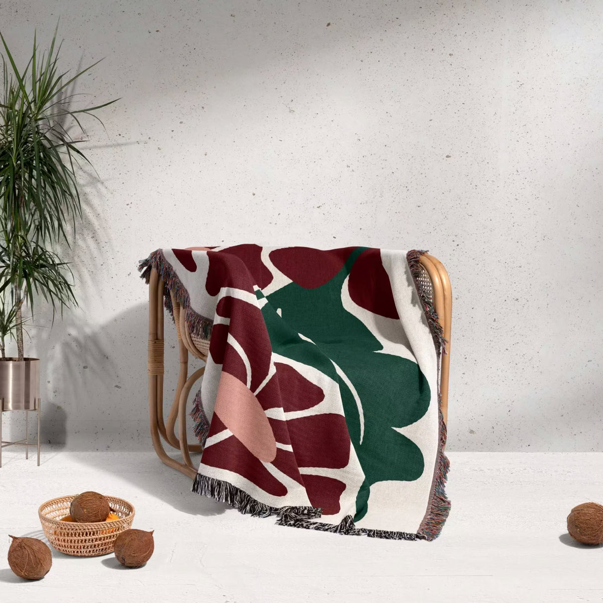 Decorative Matisse style botanical cotton woven throw blanket with leaf pattern draped over a chair against a light gray wall.