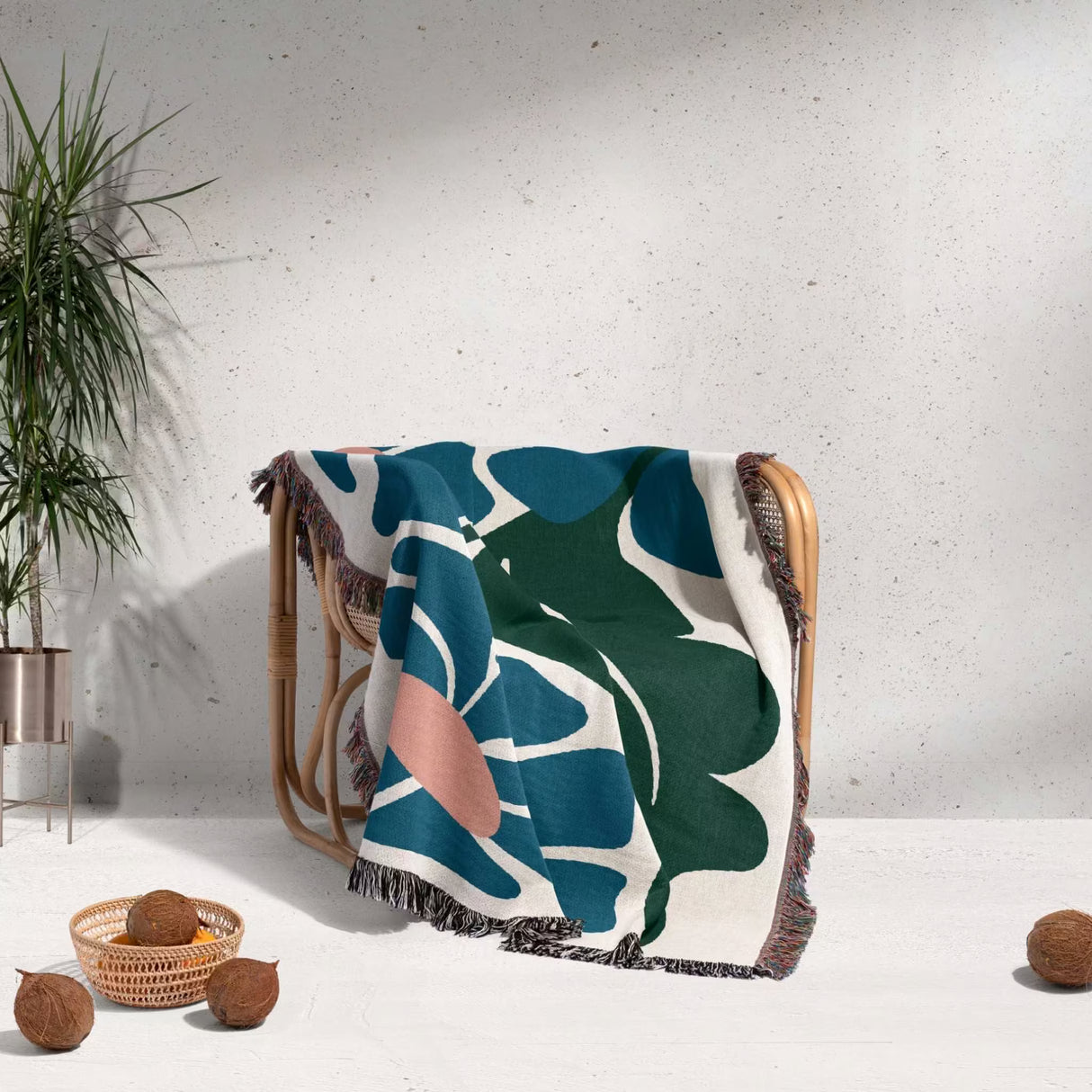 Decorative Matisse style floral cotton woven throw blanket for couch with leaf pattern draped over a chair against a light gray wall.