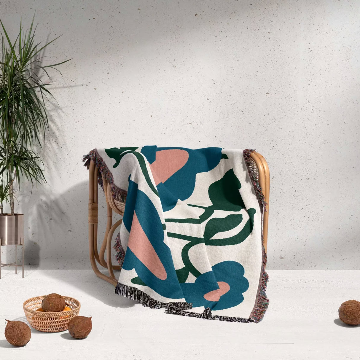 Colorful floral-patterned Matisse style flowers cotton woven throw blanket draped over a chair against a light gray wall.