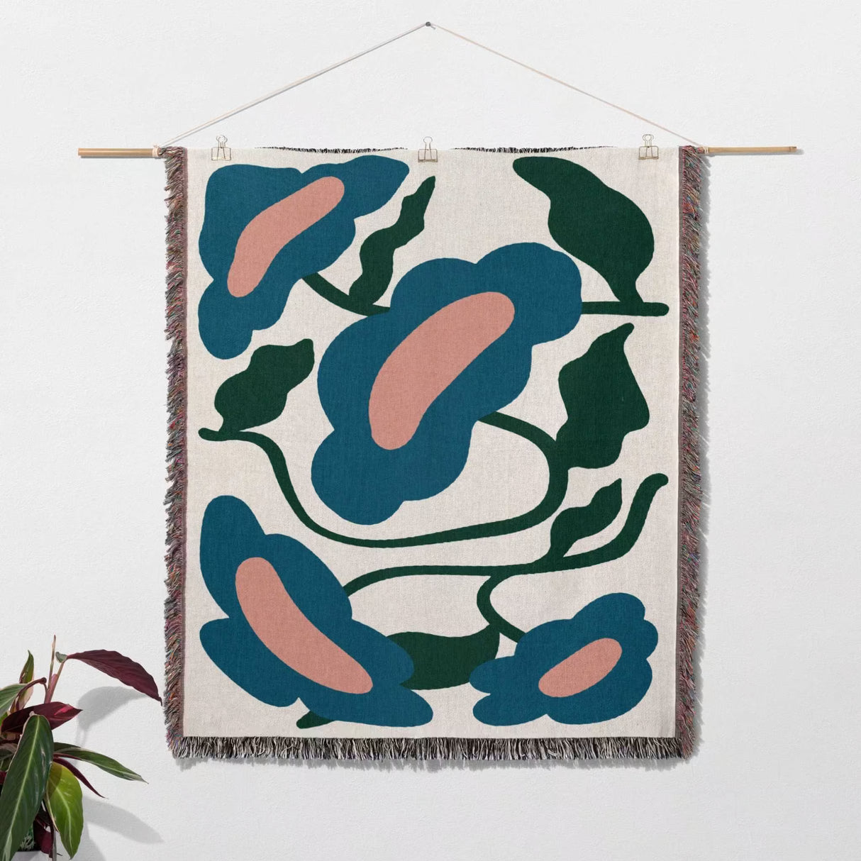 Matisse style flowers cotton woven throw blanket as a wall art tapestry hanging on a white wall with a plant on the side.