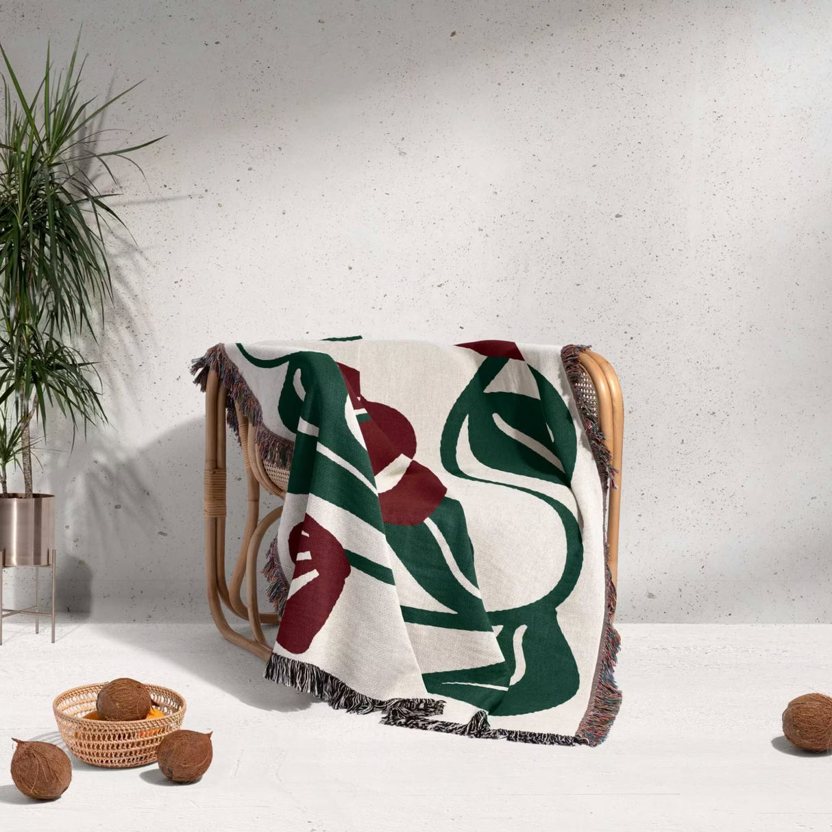 Decorative Matisse style red floral cotton woven throw blanket with leaf pattern draped over a chair against a light gray wall.