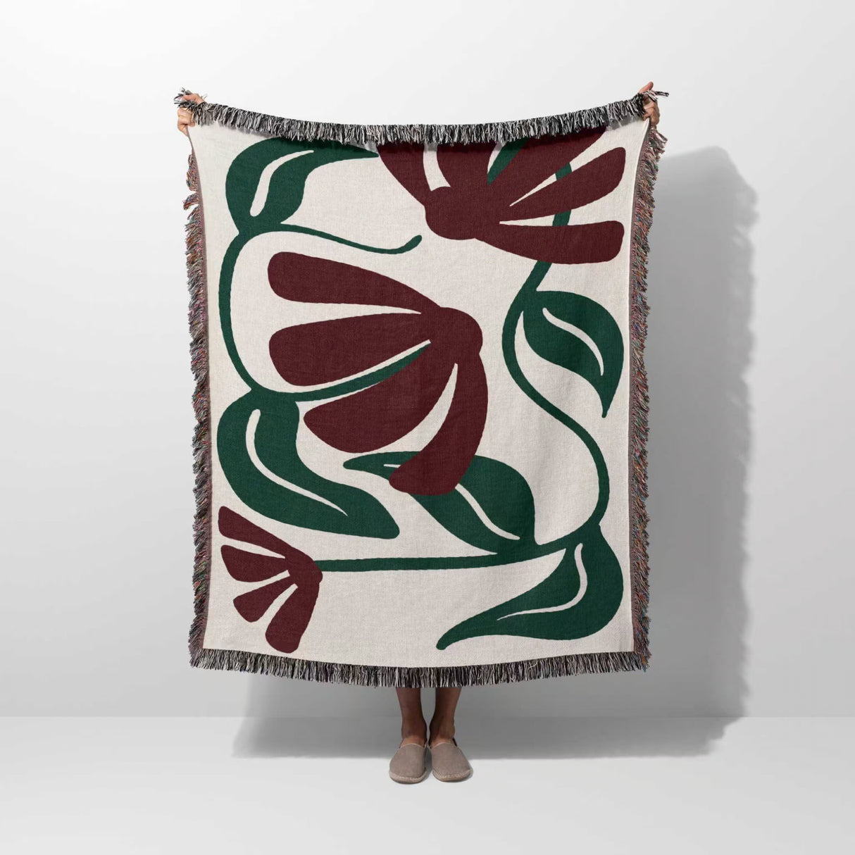Floral patterned Matisse style red floral cotton woven throw blanket draped over a person on a white background