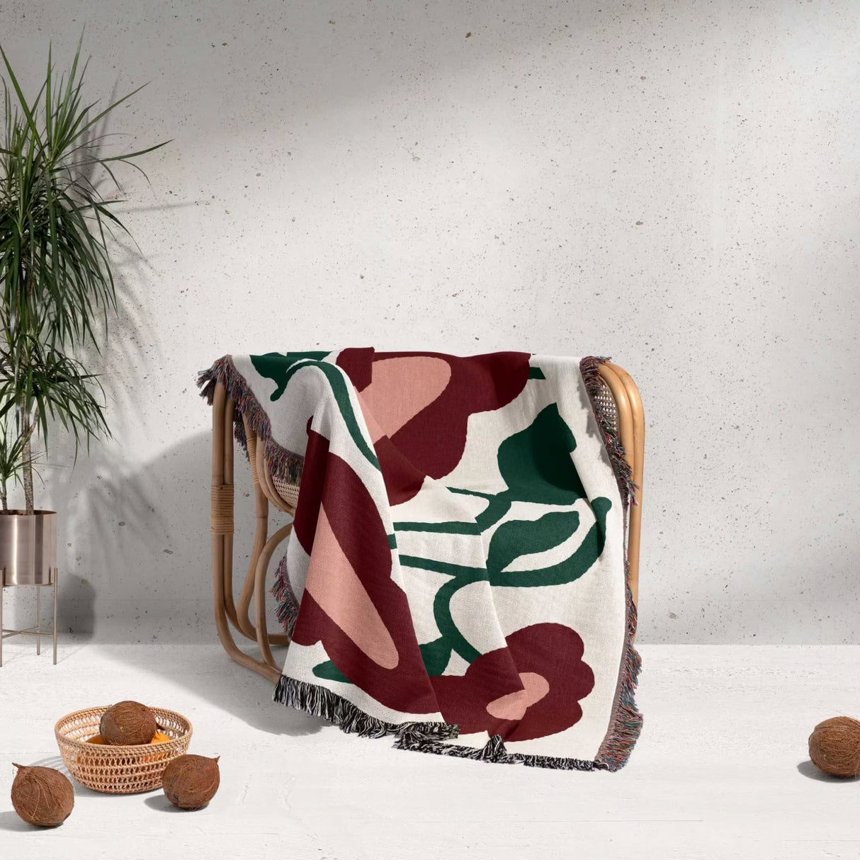 Floral-patterned Matisse style red flowers cotton woven throw blanket draped over a chair against a light gray wall with decorative elements.