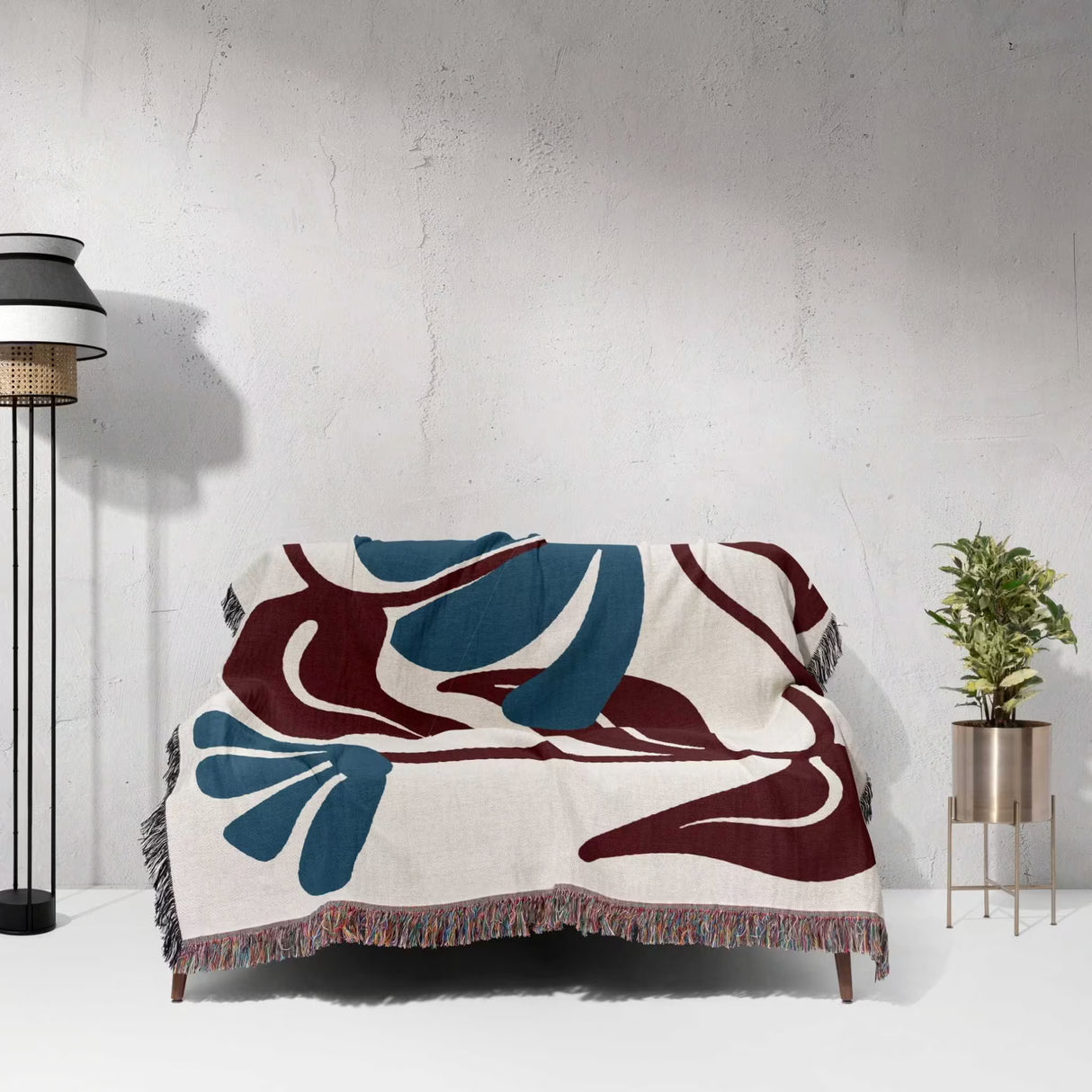 Decorative Matisse style red and blue cotton woven throw blanket with abstract design on a white surface, with a lamp and plant in the background.