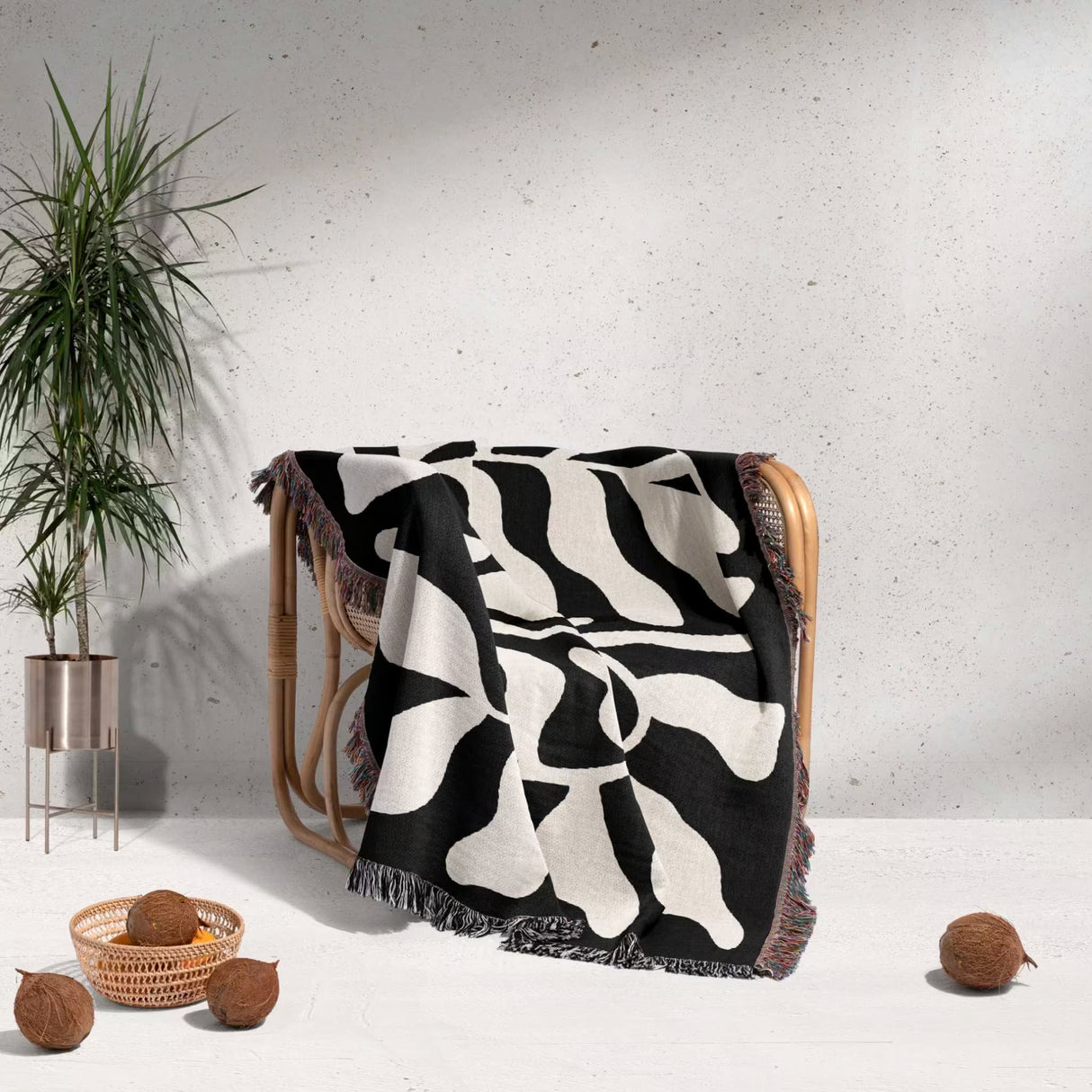 Black leaf Matisse throw blanket draped over a chair with a plant and coconuts in the background.