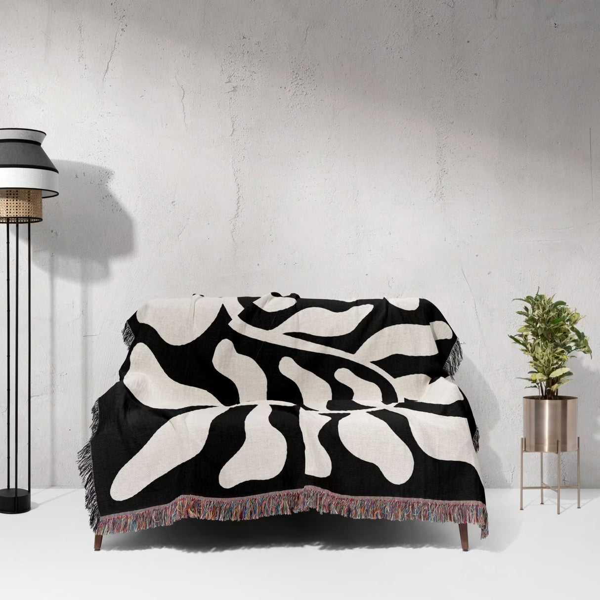 Black leaf Matisse throw blanket draped over a couch against a light gray wall.