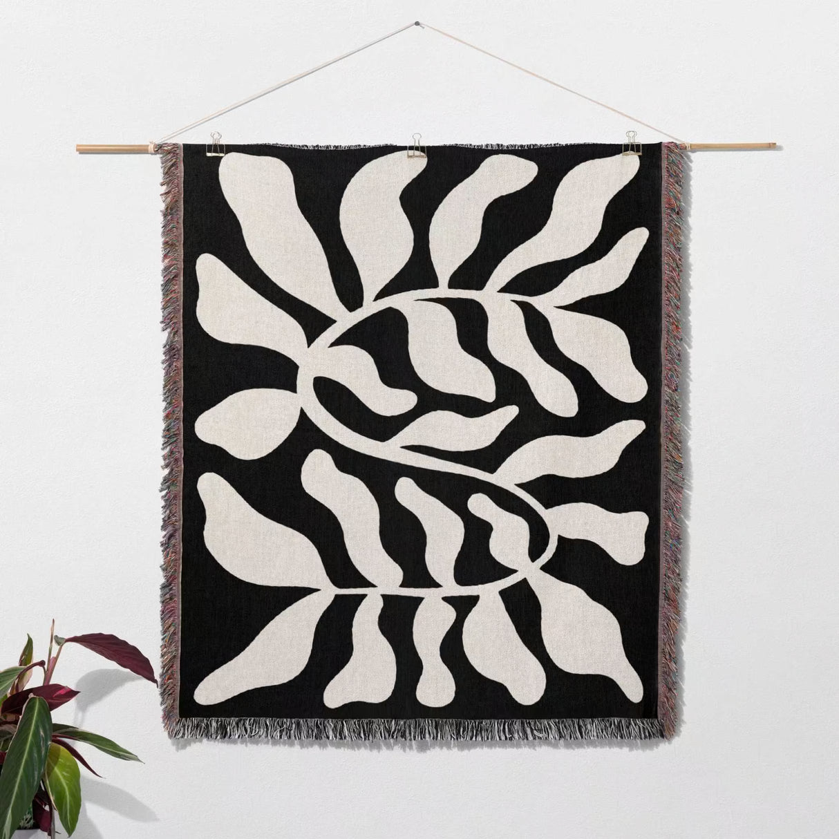Black leaf Matisse throw blanket as woven wall art hanging with abstract leaf pattern on a black background, hanging on a white wall.
