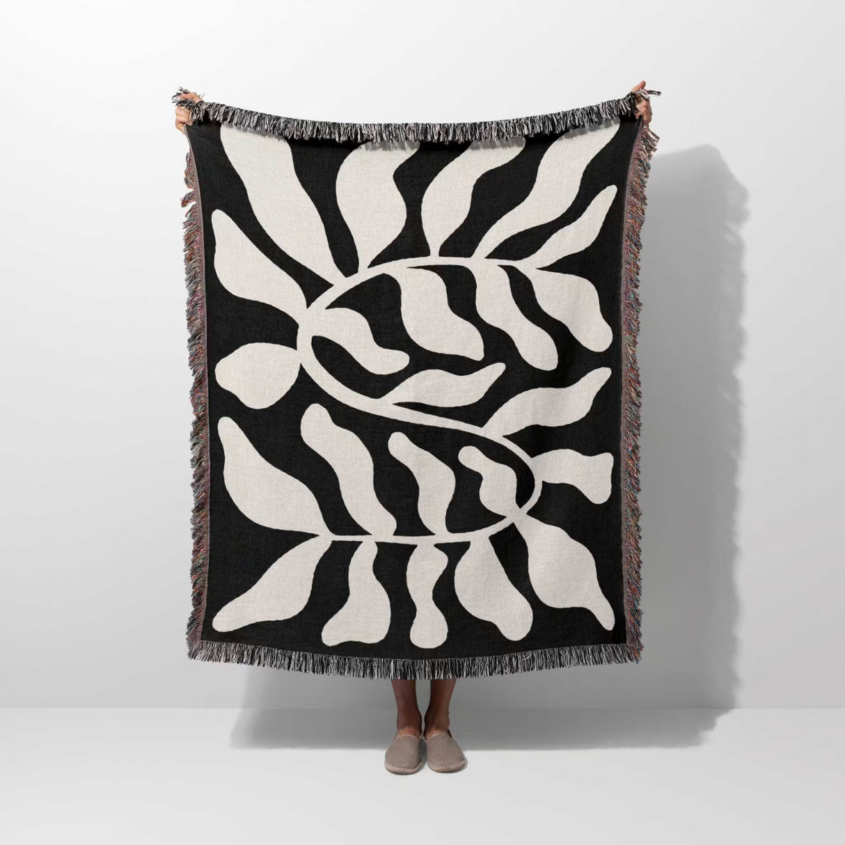 Black leaf Matisse throw blanket held up by a person on a white background