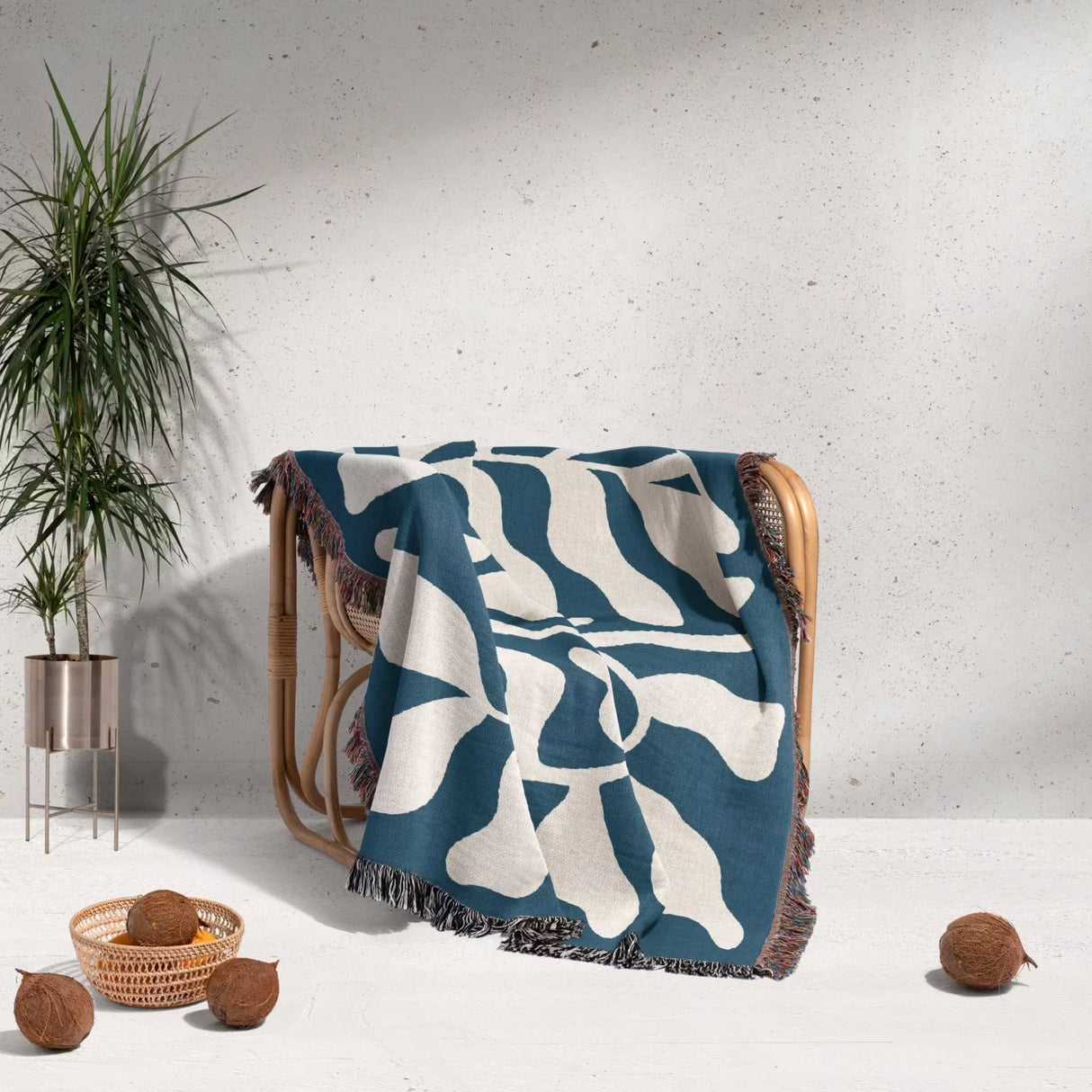 Blue leaf abstract woven Matisse trow blanket tapestry draped over a wooden chair with a plant and coconuts in the background.