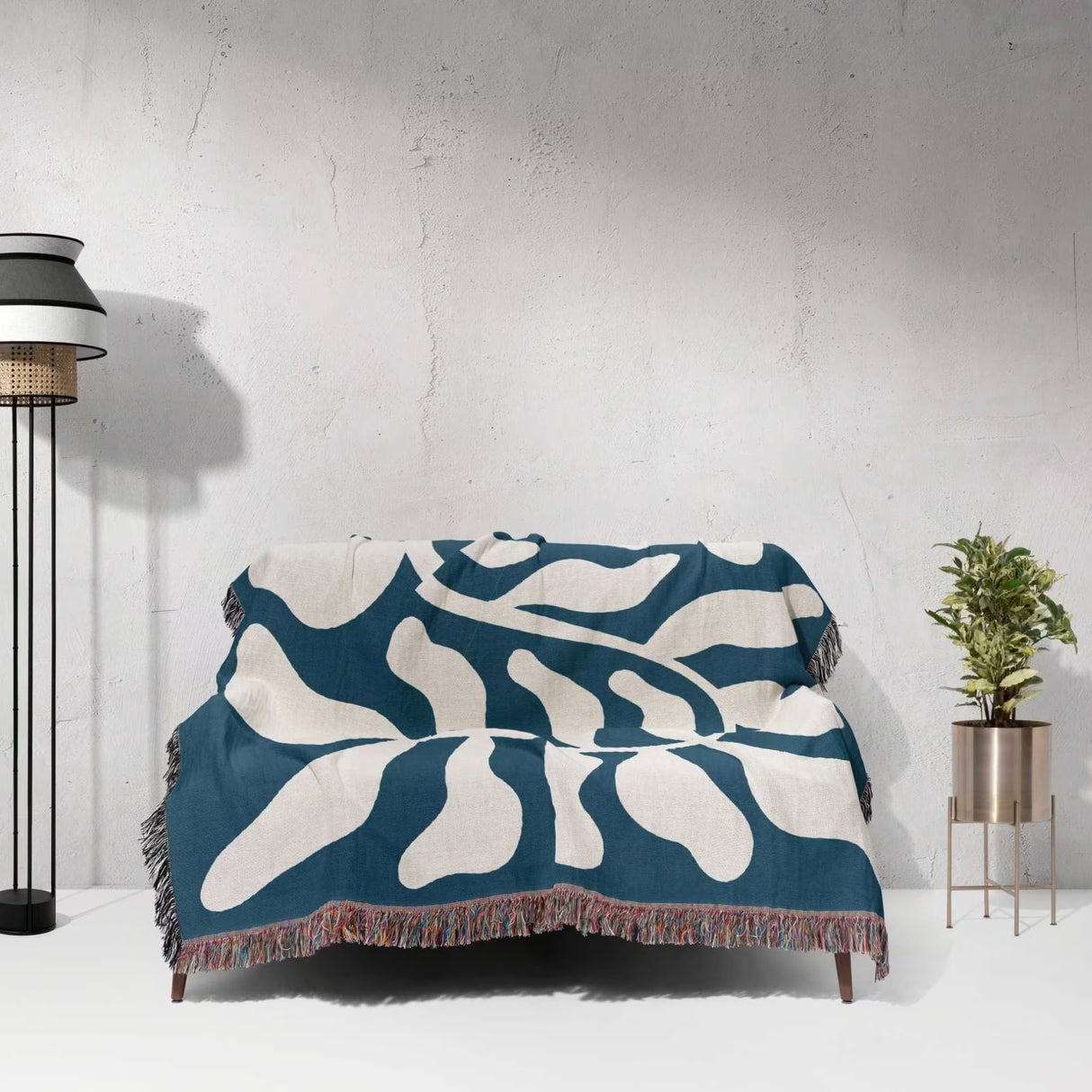 Blue leaf abstract woven Matisse trow blanket tapestry draped over a couch against a white wall.