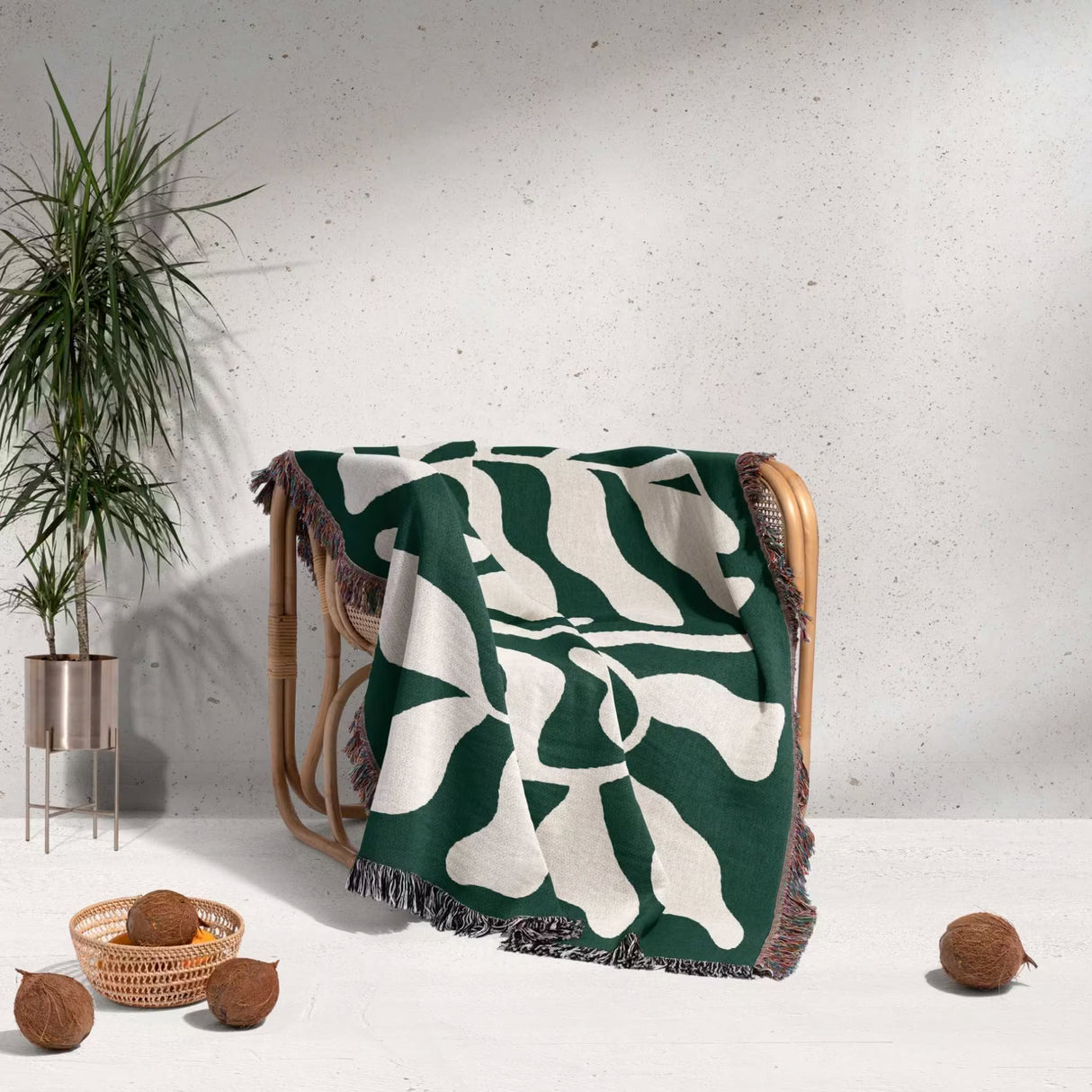 Matisse throw blanket green leaf abstract tapestry draped over a chair with a plant and coconuts in the background.