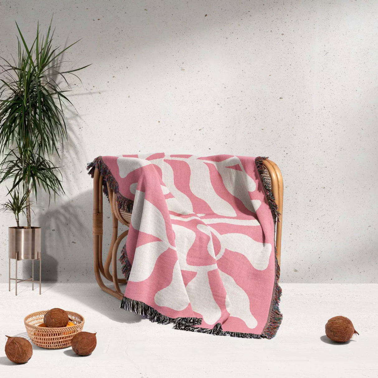 Lighter red abstract Matisse throw blanket draped over a wooden chair with a plant and coconuts in the background.