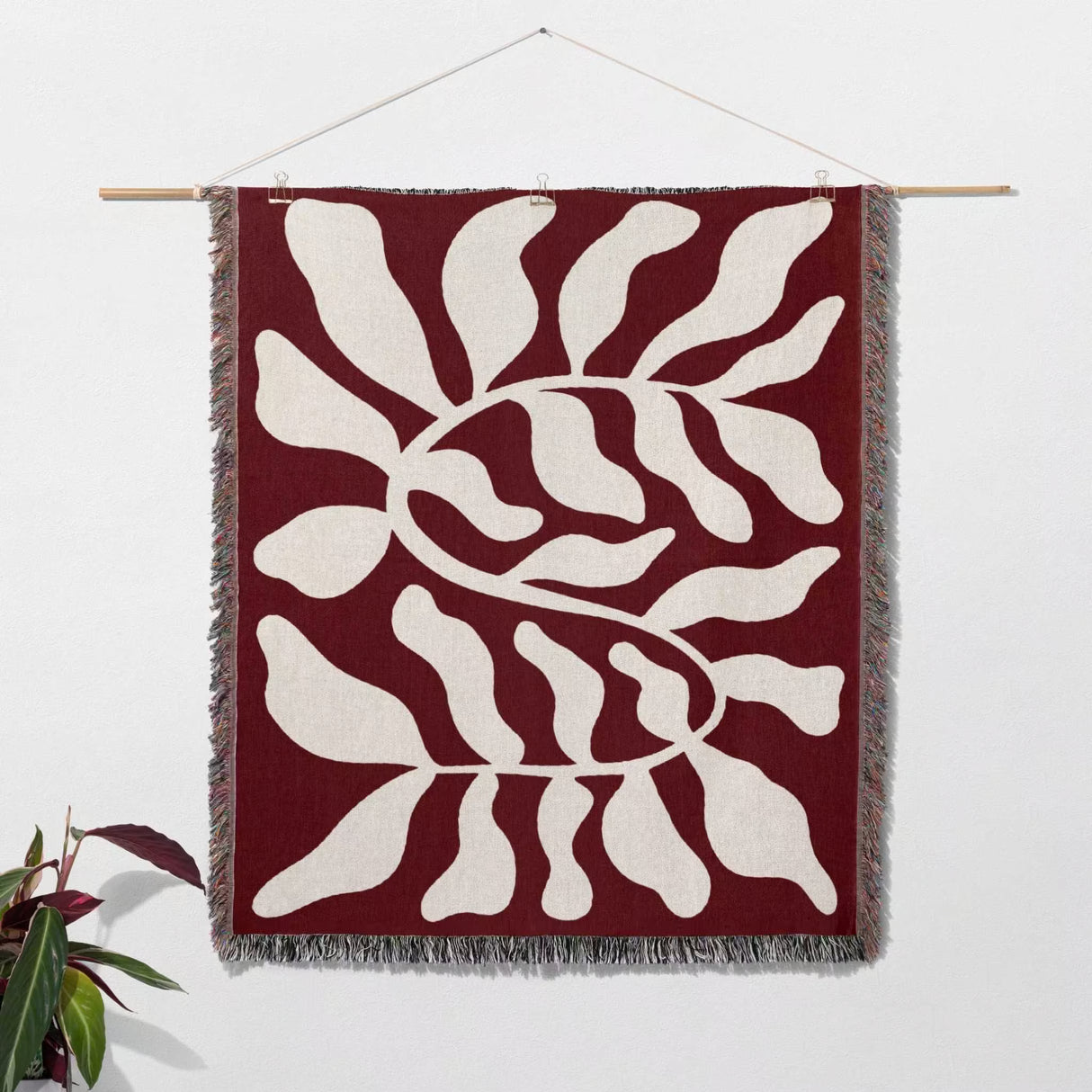 Red leaf abstract Matisse throw blanket as a Woven wall art hanging on a white wall.