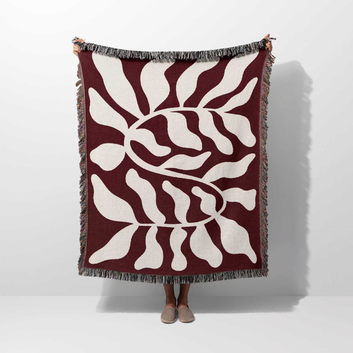 Red leaf abstract Matisse throw blanket held up by a person on a white background