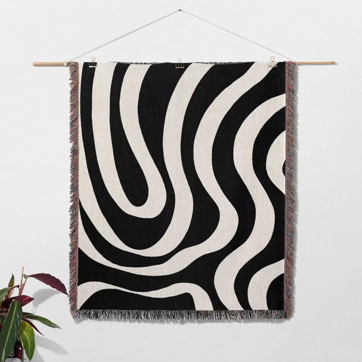 Black and white modern abstract woven blanket throw tapestry hanging on a wall with a plant in the corner.