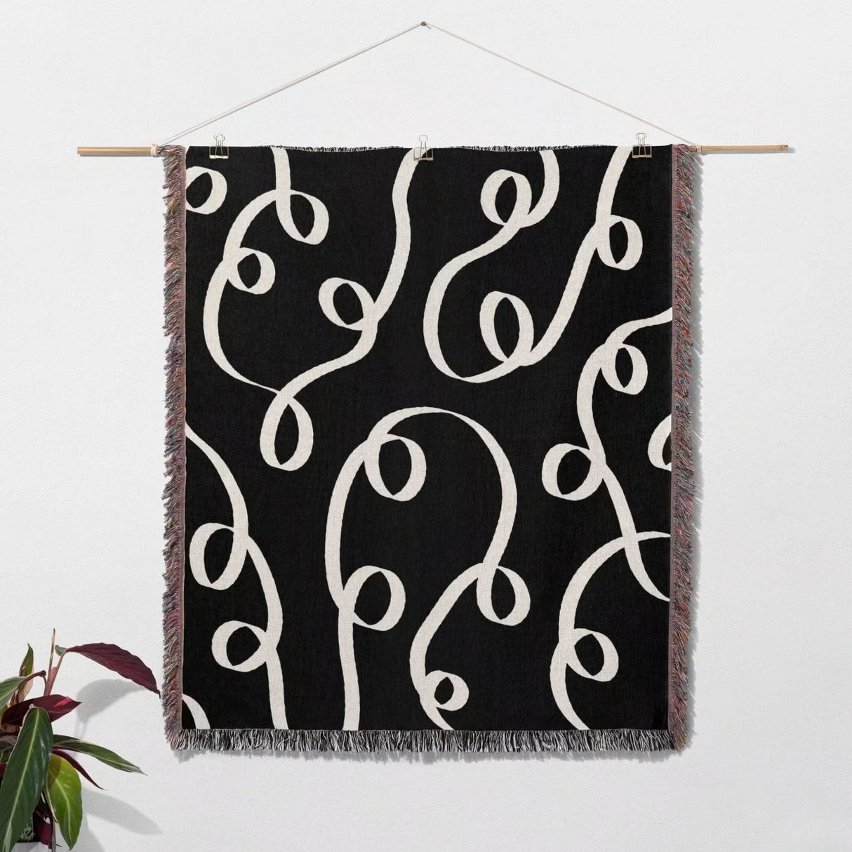 Black and white modern accent woven blanket throw tapestry hanging on a wooden rod against a white wall.