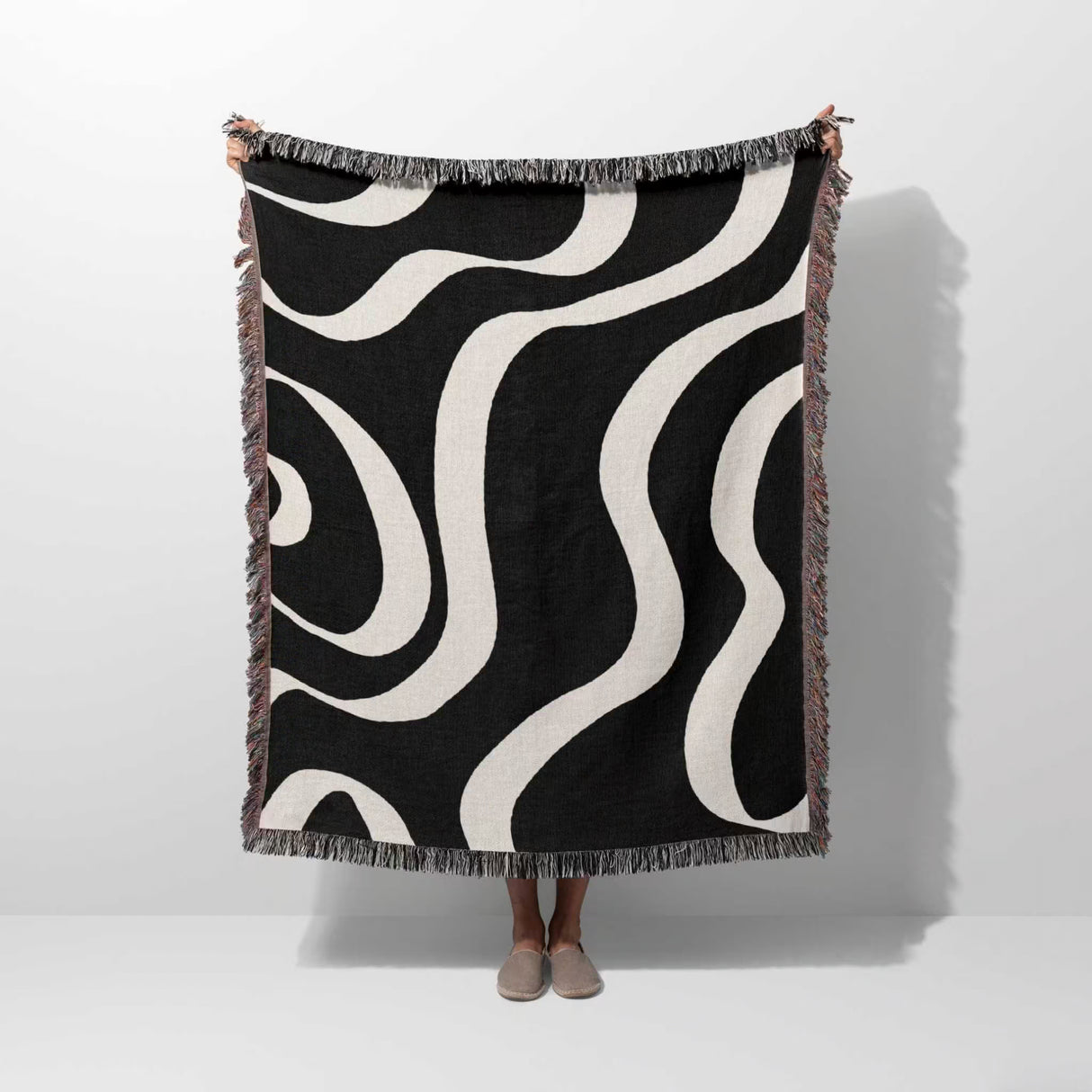 Black and white modern aesthetic waves woven blanket throw held by a person on a white background.