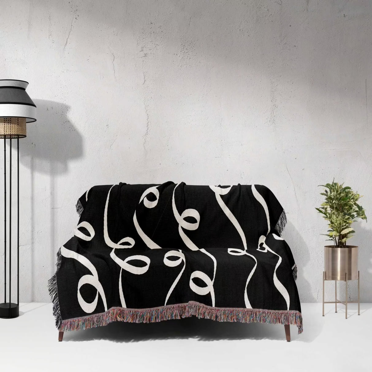 Black and white modern art decorative woven blanket throw tapestry draped over a sofa against a white wall.