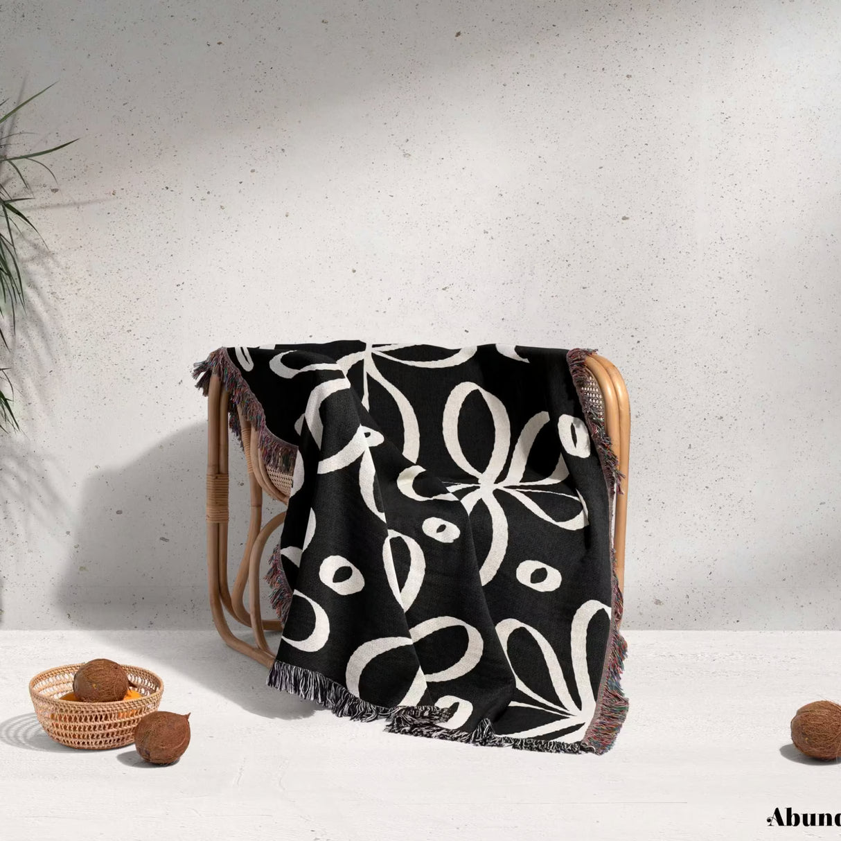 Black and white modern artsy flowers woven blanket throw draped over a chair against a light gray wall.