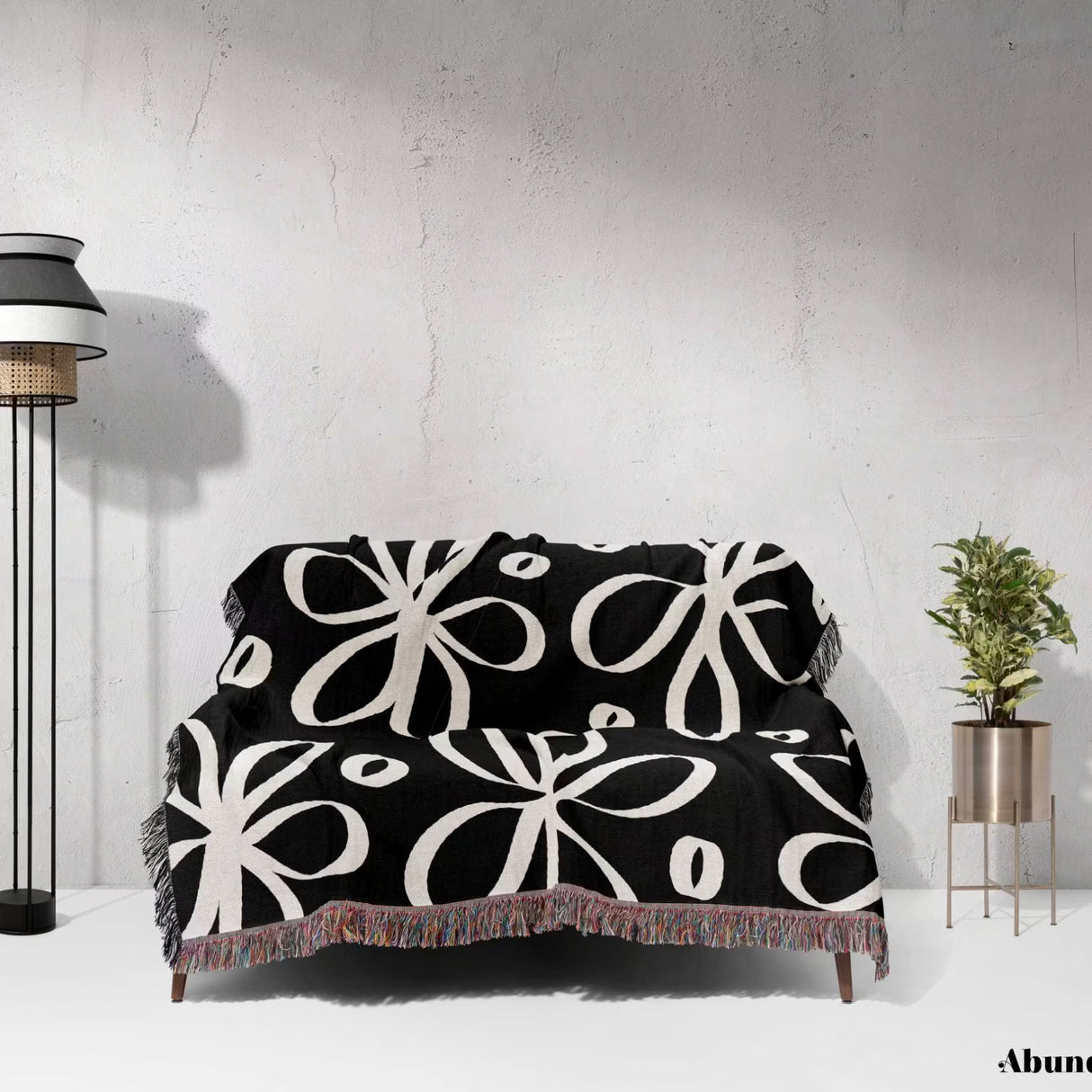Black and white modern artsy flowers woven blanket throw draped over a couch against a white wall.