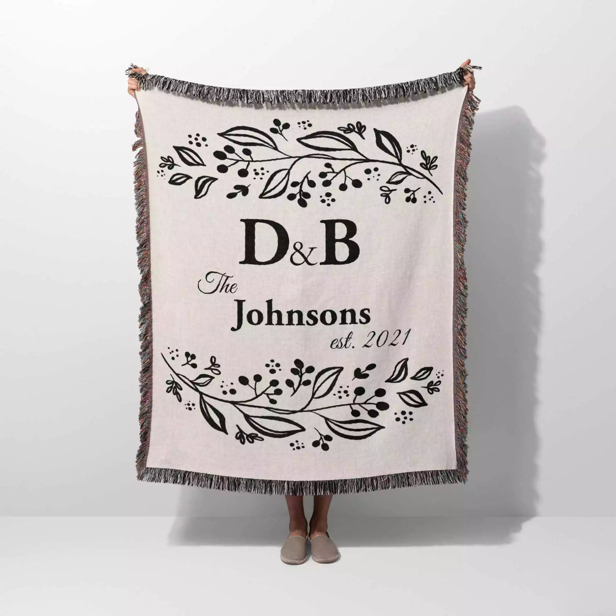 Monogrammed cotton throw blanket perfect engagement and wedding gift held by a person on a white background