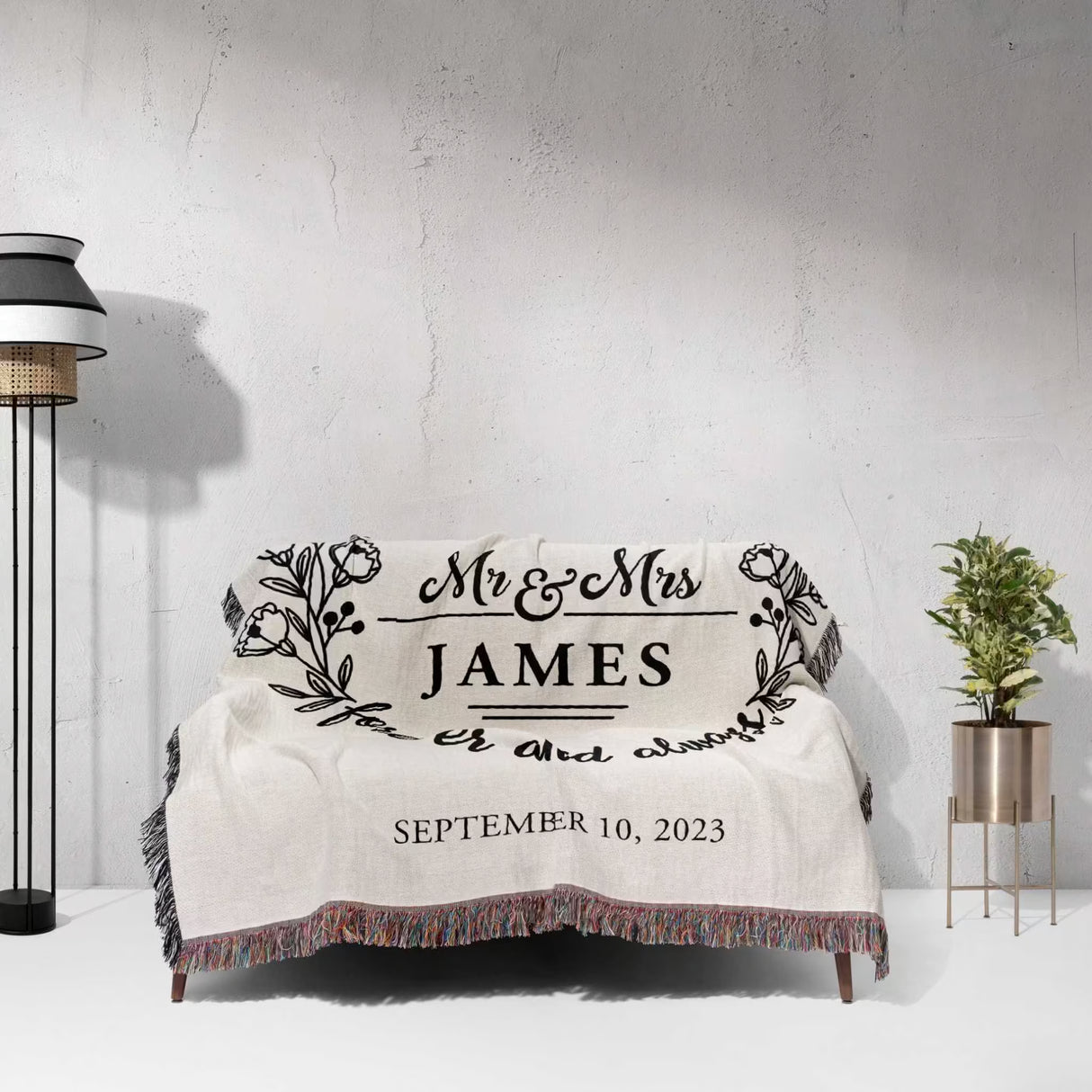 Mr and Mrs cotton wedding anniversary gift woven blanket with 'Mr & Mrs James' and wedding date on a couch against a light gray wall.