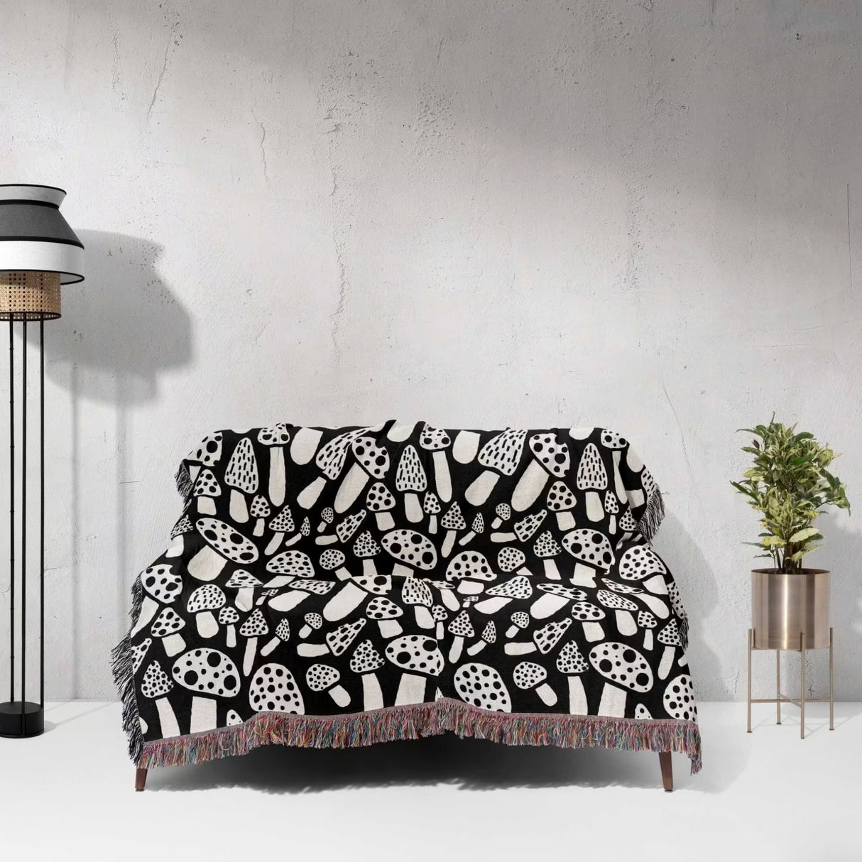 Black and white mushrooms patterned woven blanket throw draped over a sofa against a white wall.