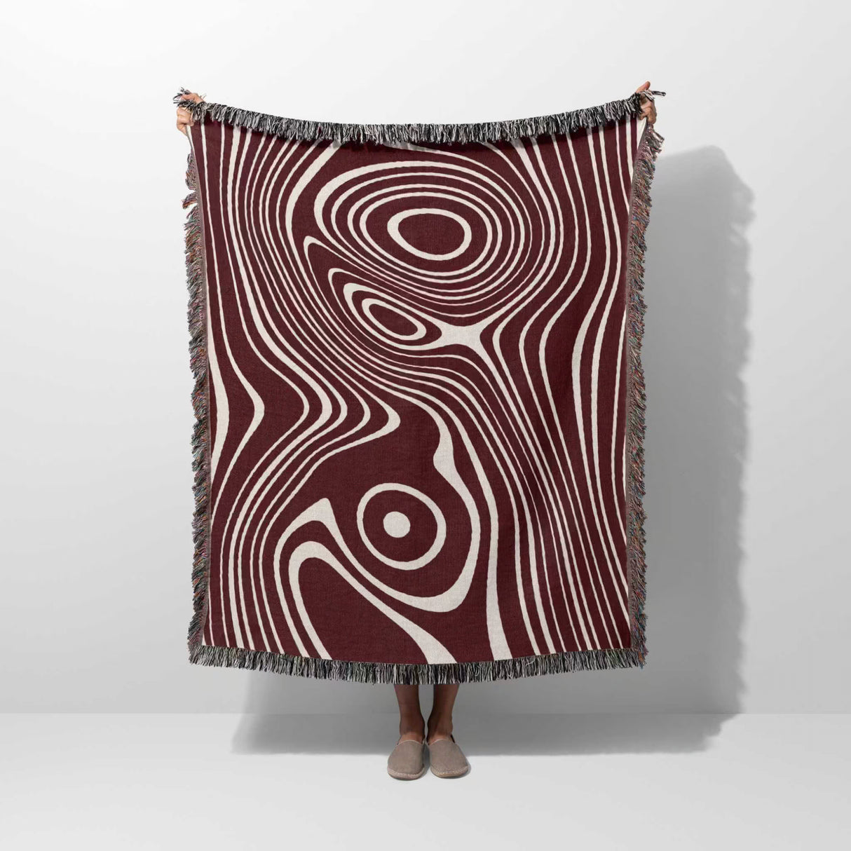 Person holding a patterned red abstract woven throw blanket with concentric circle design on a white background