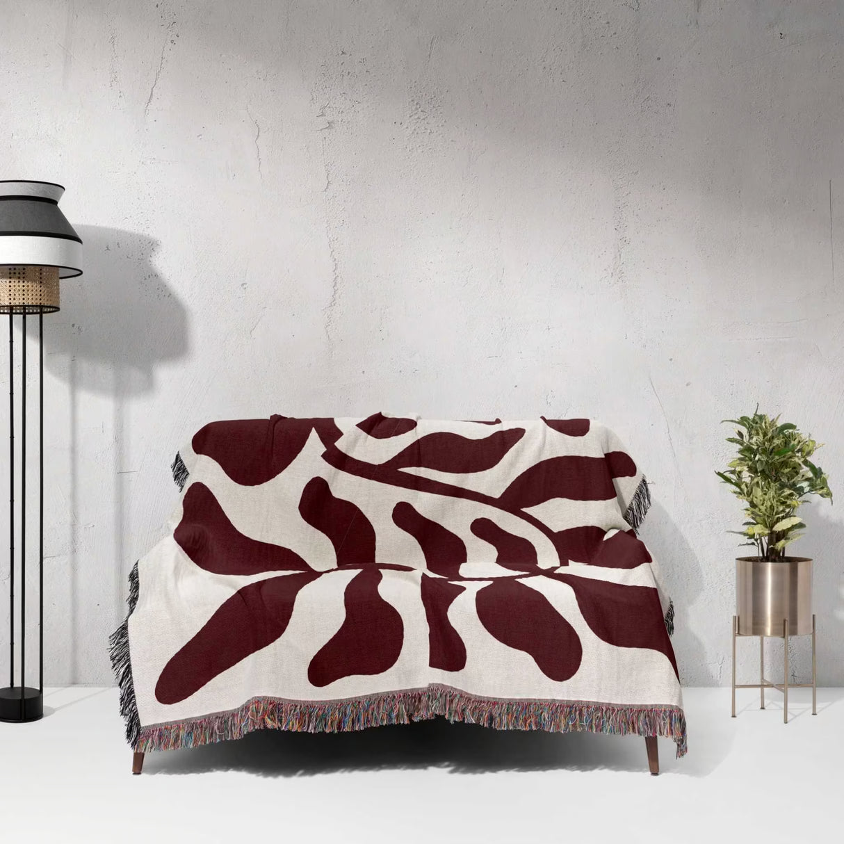 Red leaf Matisse throw blanket draped over a couch against a light gray wall.
