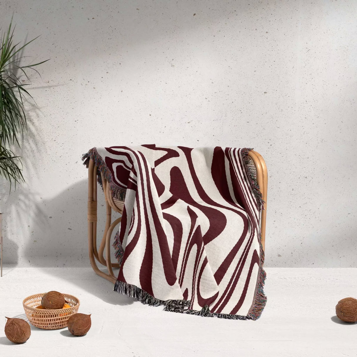 Red marble woven throw blanket for couch draped over a wooden chair against a white wall.