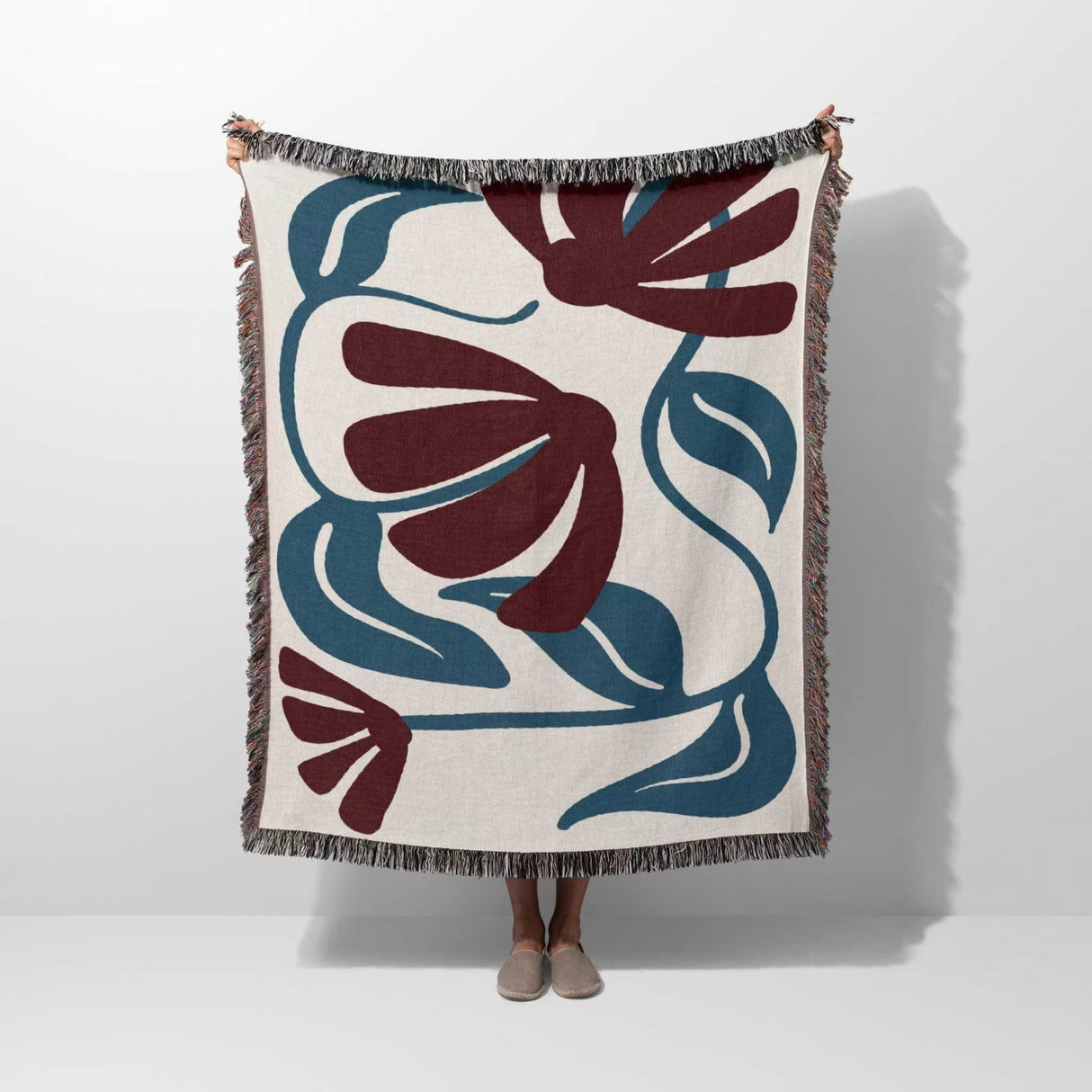 Person holding a red and blue Matisse tapestry throw blanket with floral pattern on a white background
