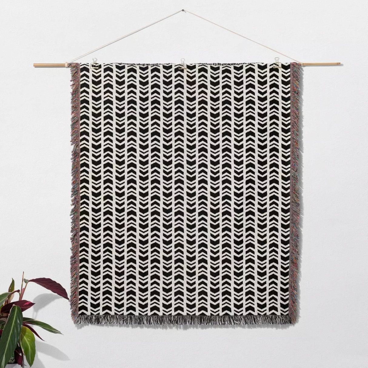 Black and white retro arrow lines woven blanket throw tapestry with fringe hanging on a wooden rod against a white wall.