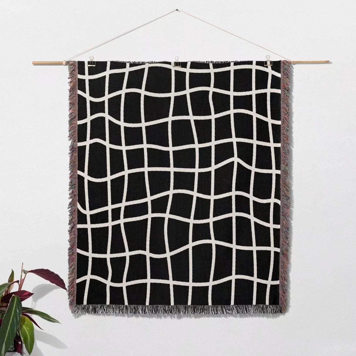 Black and white retro checkered woven blanket throw tapestry hanging on a wooden rod against a white wall.