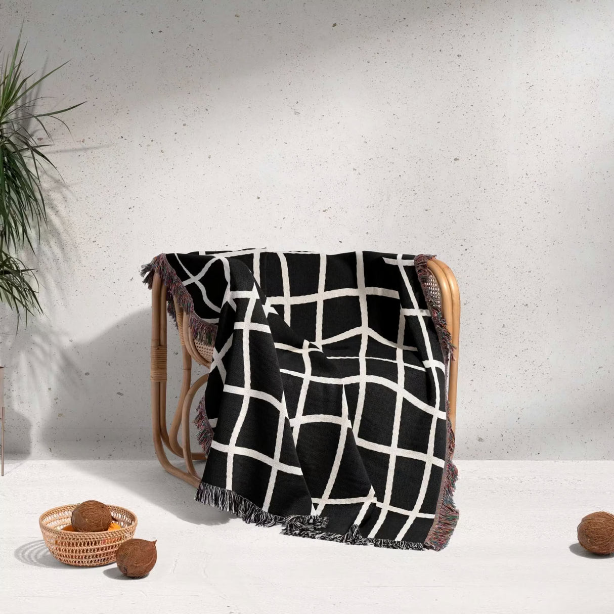 Black and white retro checkered woven blanket throw tapestry draped over a wooden chair against a light gray wall.