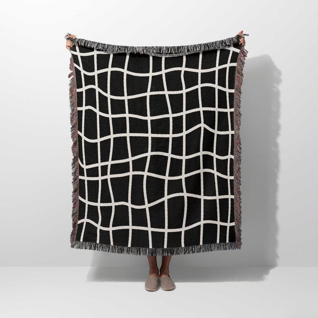 Black and white retro checkered woven blanket throw tapestry held by a person on a white background.