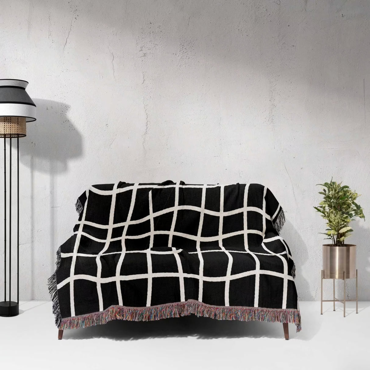 Black and white retro checkered woven blanket throw tapestry draped over a sofa against a white wall.