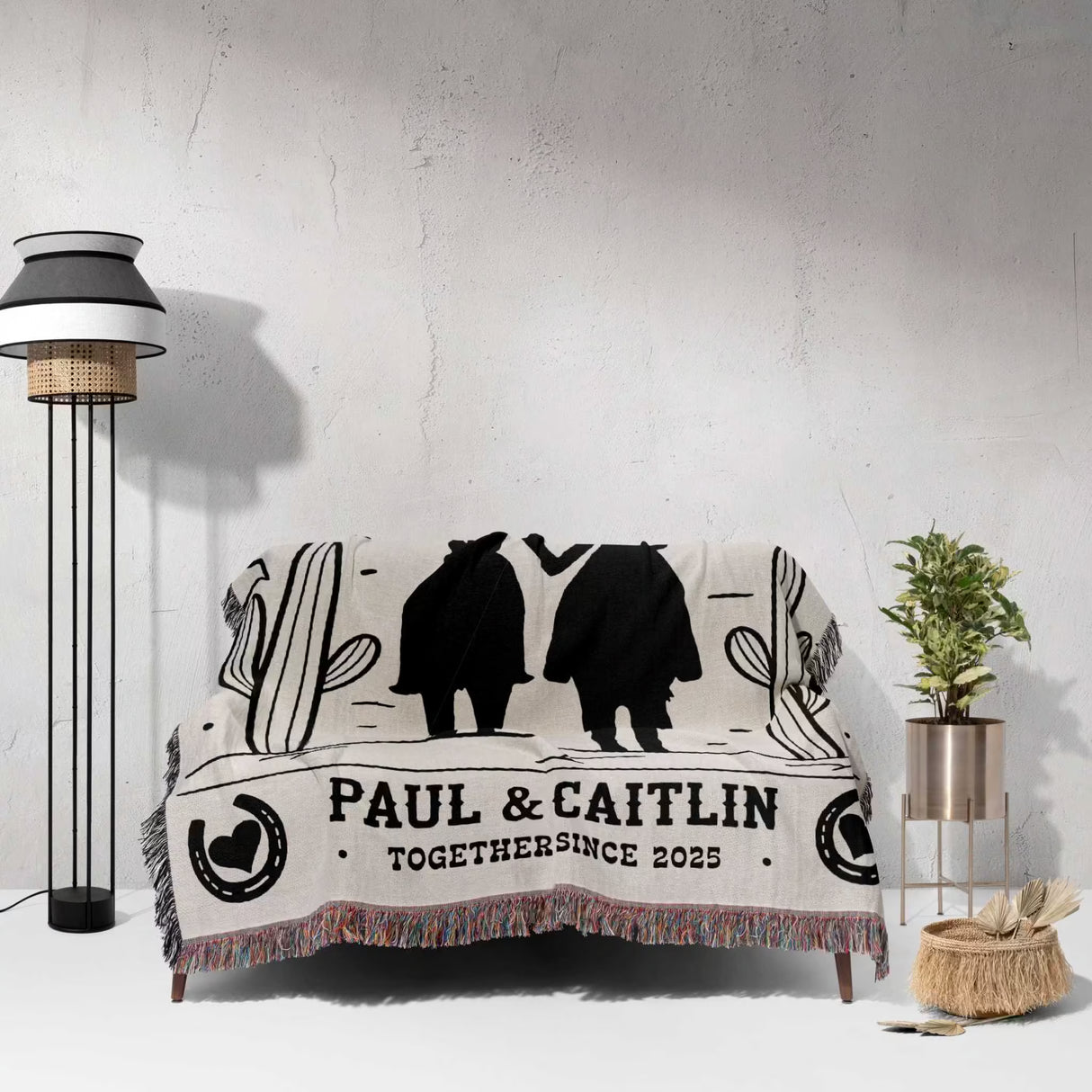 Romantic cowboy and cowgirl cotton anniversary gift – woven throw blanket with silhouettes of a couple and text 'PAUL & CAITLIN TOGETHER SINCE 2023' draped over a couch in a room.