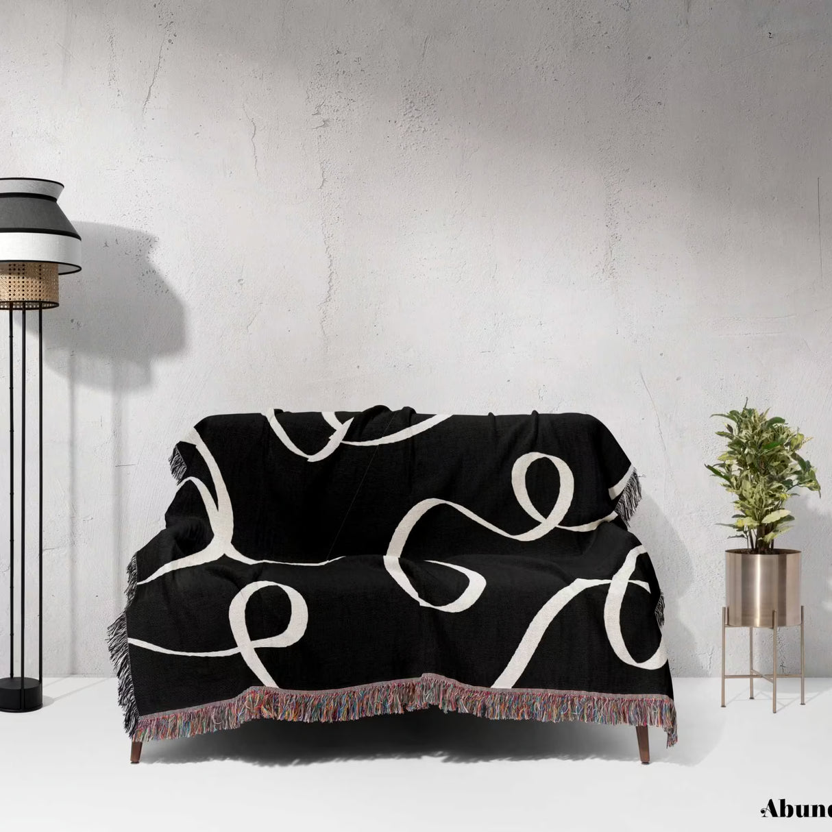 Black and white scribble lined woven blanket throw with fringe draped over a couch against a white wall.