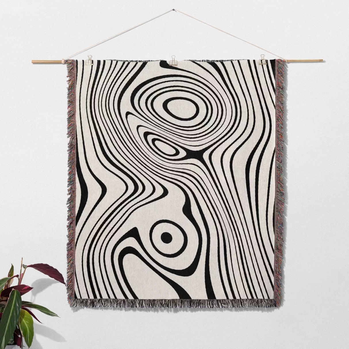 Simple black and white modern couch woven throw blanket as Woven tapestry with black and white abstract pattern hanging on a white wall.